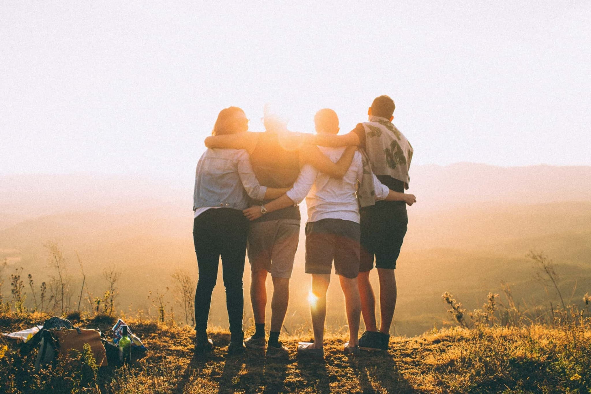 Friends standing with their arms around one another in warm sunset light.